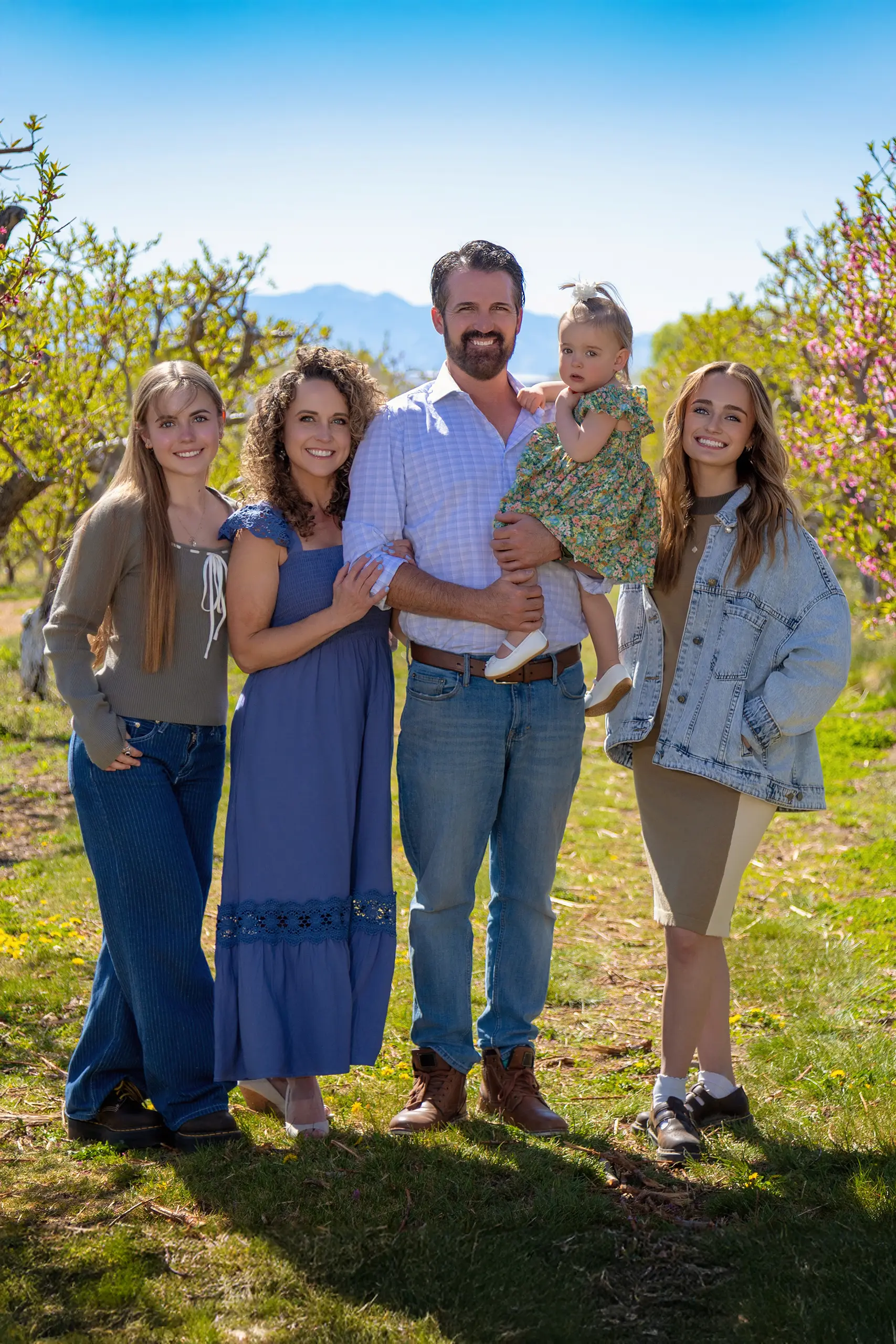 A large family posing together in a sunny mountain field with colorful blossoms during an Ogden, Utah portrait session.