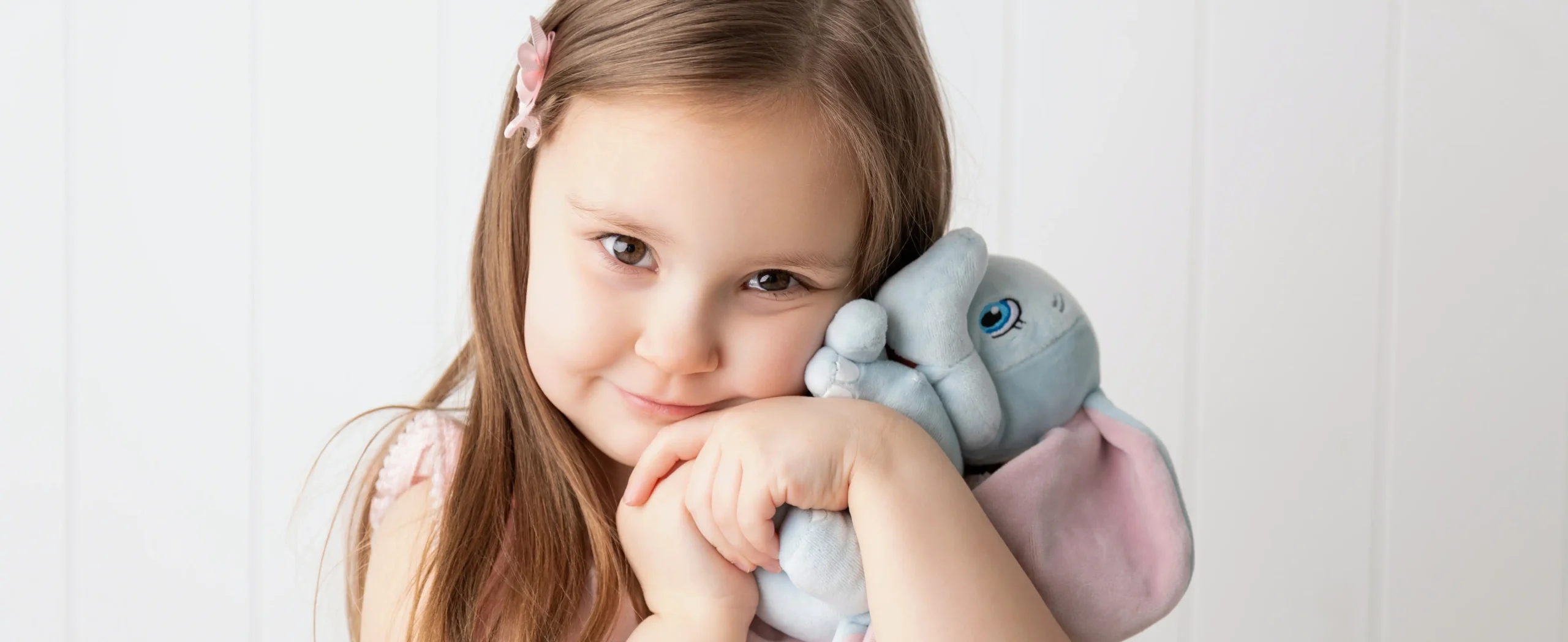 Children's portrait photography in Ogden Utah featuring a young girl hugging a soft elephant plush toy with natural window lighting.
