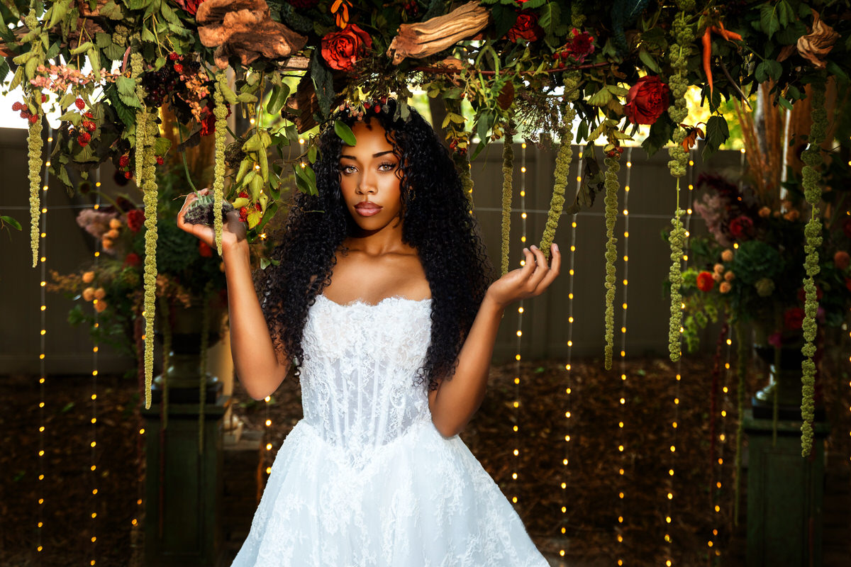 Portrait of a bride holding a unique floral arrangement with rich autumn tones and artichokes by Lund Floral, showcasing a strapless lace gown from Just Girl Stuff during a styled shoot by Masterpiece Images in Ogden, Utah.