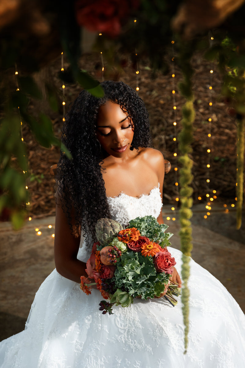 Stunning bride in a strapless lace gown from Just Girl Stuff holding a bridal bouquet with lush greenery and artichokes by Lund Floral during a styled shoot at Eldridge Manor in Ogden, Utah, captured by Masterpiece Images.