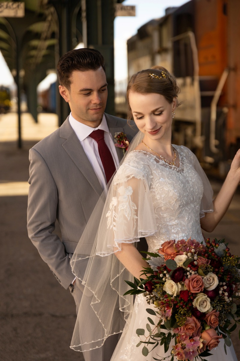 Bride and groom standing together near a historic train at Ogden Union Station.