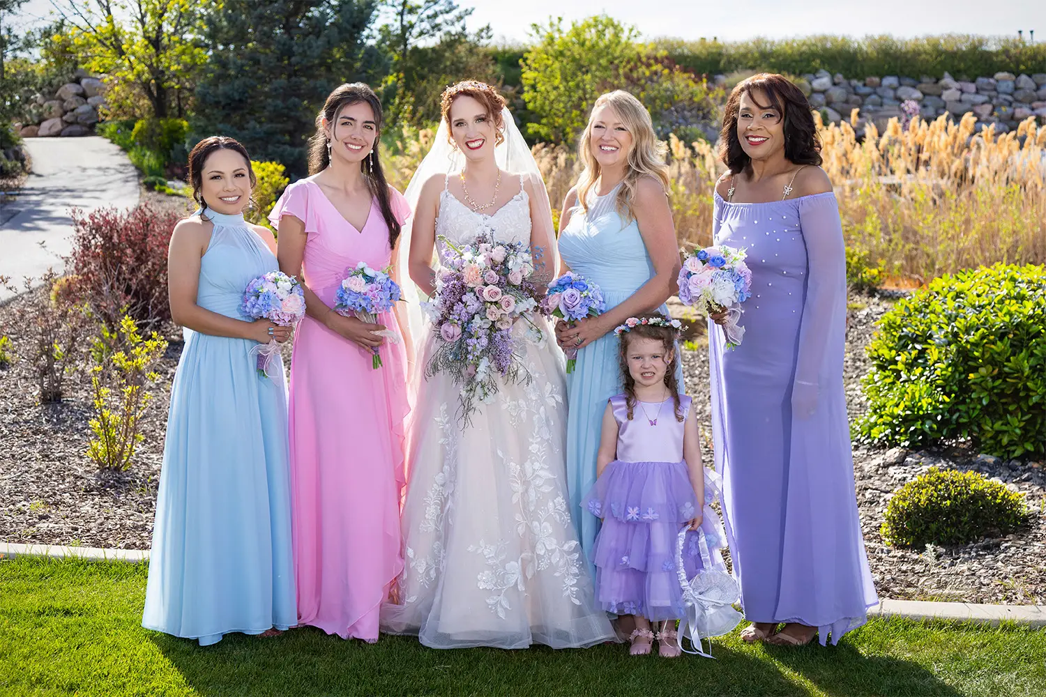 Bridesmaids in purple dresses and the bride in a white gown posing outdoors on a lawn