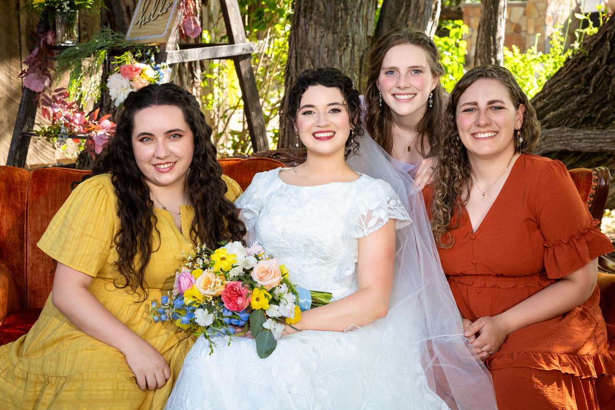 Bride and three bridesmaids in matching dresses posing together outdoors in a lush, green setting.
