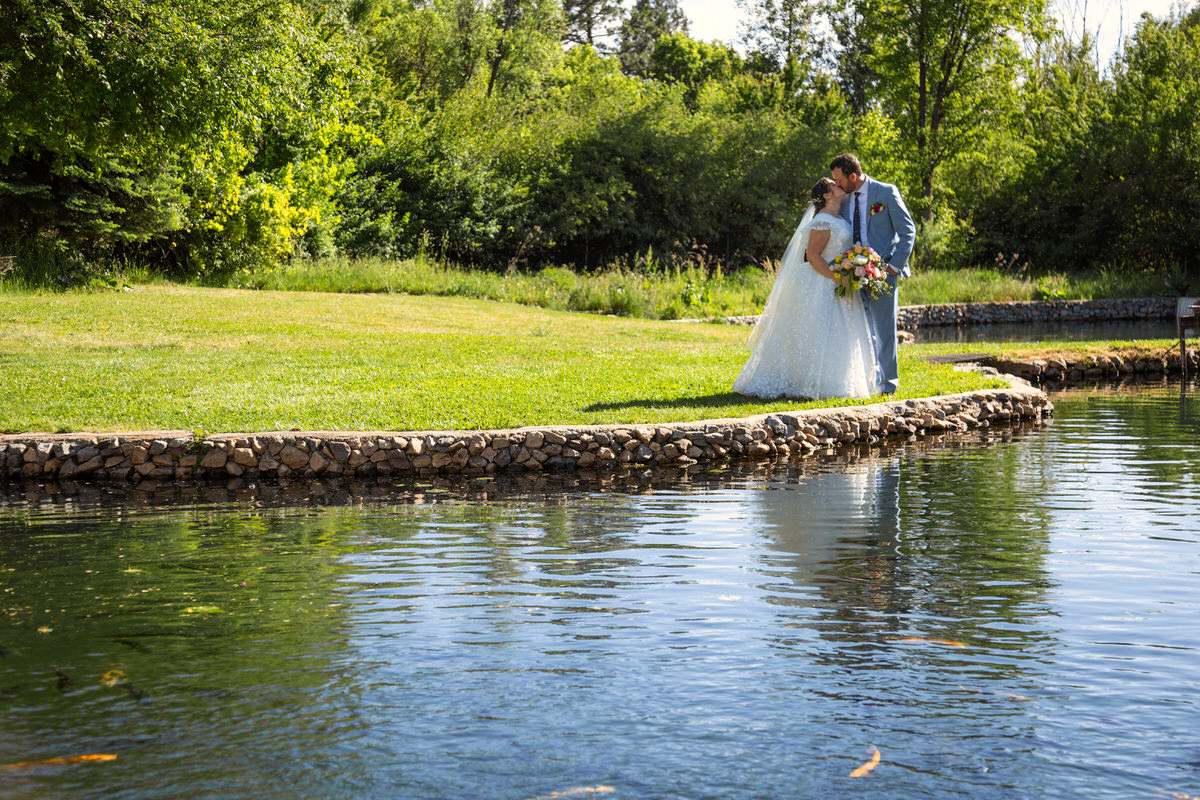 Bride and groom sharing a romantic kiss outdoors in a lush, green natural setting with soft sunlight.