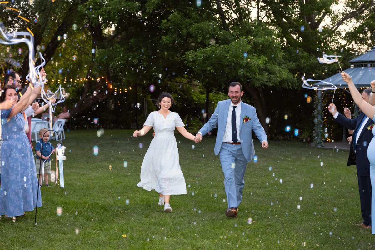 Bride and groom walking outside through a cascade of celebratory bubbles blown by wedding guests.