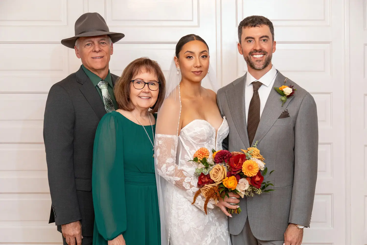 Bride and groom standing indoors in front of a wooden door with family members