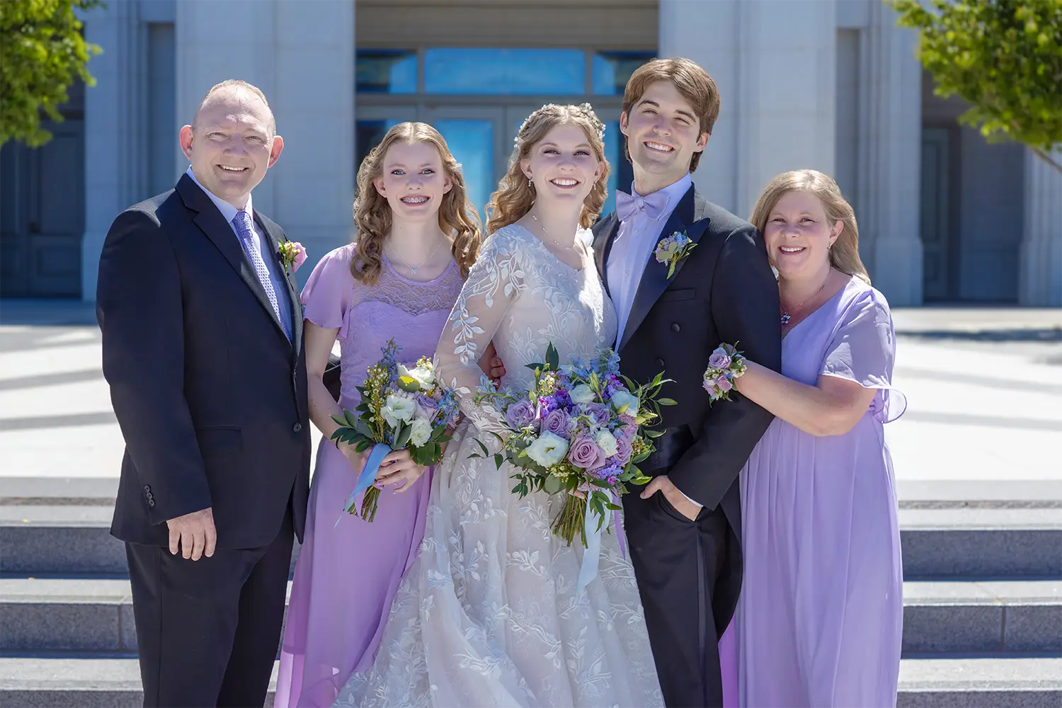 Bride, groom, and family members posing together outdoors on a stone patio in front of a building