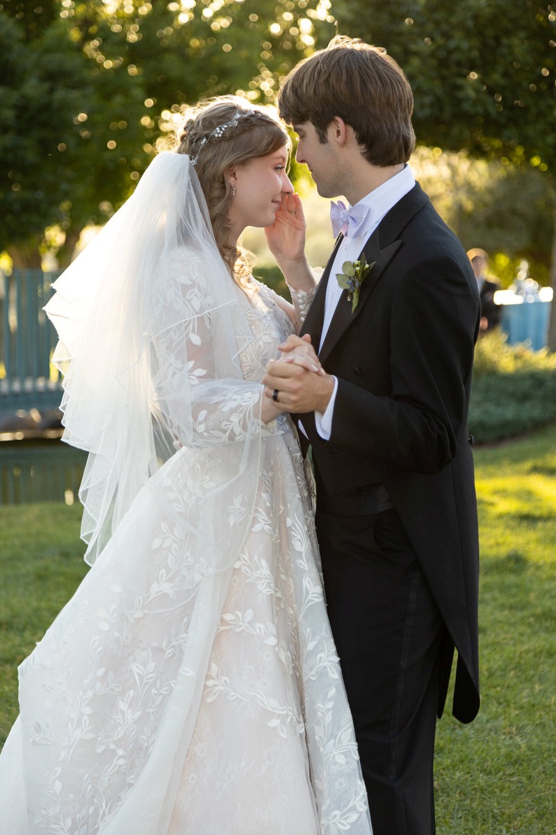 Bride and groom dancing outdoors in the sunlight, with the bride gently touching the groom's face.