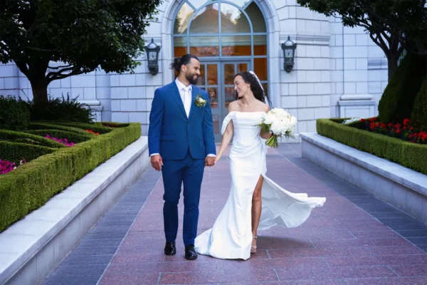 Full length wedding day portrait of bride and groom holding hands