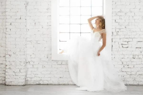 Bride posing indoors in front of a white tiled wall wearing a wedding gown and veil.