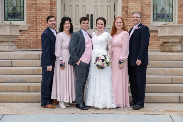 Bride and groom posing with family members outside in front of closed double doors and a brick building